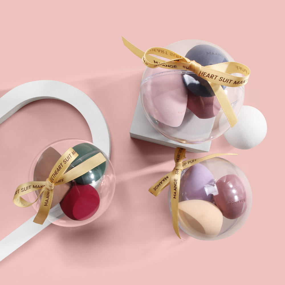 Set of multicolored soft silicone spherical beauty egg makeup sponges in clear containers tied with gold ribbons.