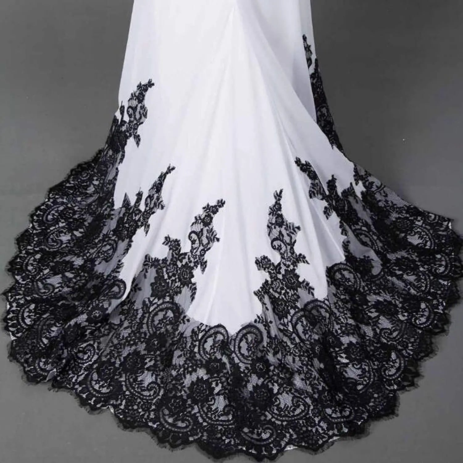 a flowing white wedding veil with intricate black lace detailing along the hem complementing a slim mermaid tail wedding dress