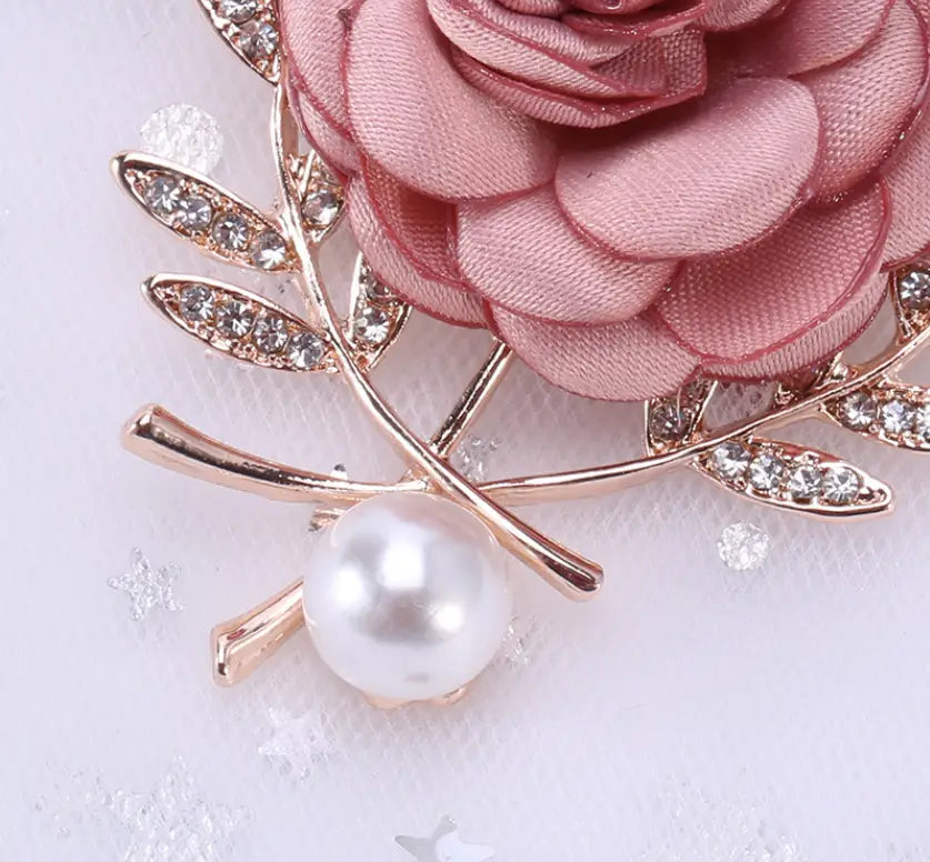A delicate fabric flower lady temperamental pin featuring a soft pink fabric rose with gold-toned rhinestone-embellished leaves and a single pearl accent.