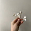 A delicate white ceramic flower pearl embellished bridal hairpin with tiny pearls and gold-toned wire stems