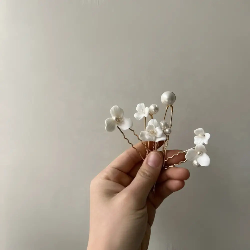 A delicate white ceramic flower pearl embellished bridal hairpin with tiny pearls and gold-toned wire stems