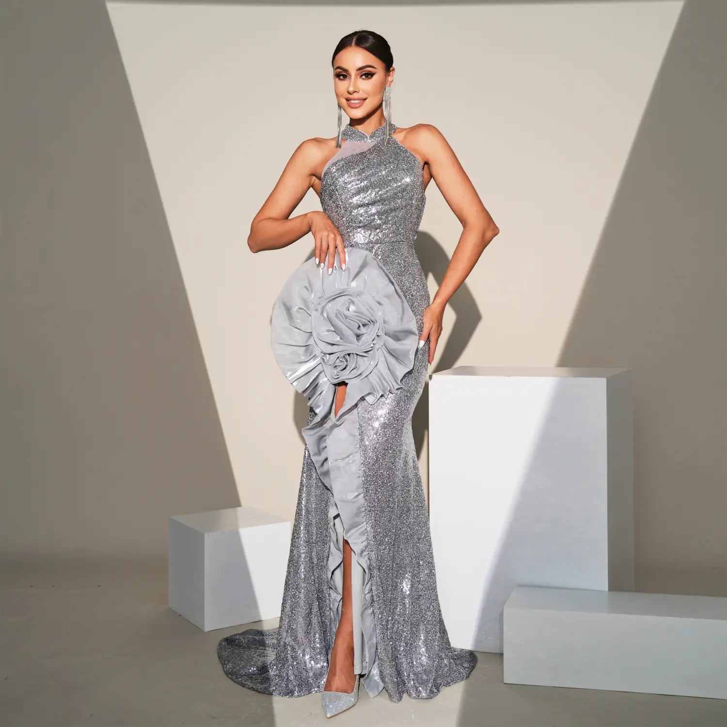A shimmering silver sequined sheath dress with a high neckline, side slit, and a large ruffled rose accent on the hip perfect for a banquet sequined sheath occasion.