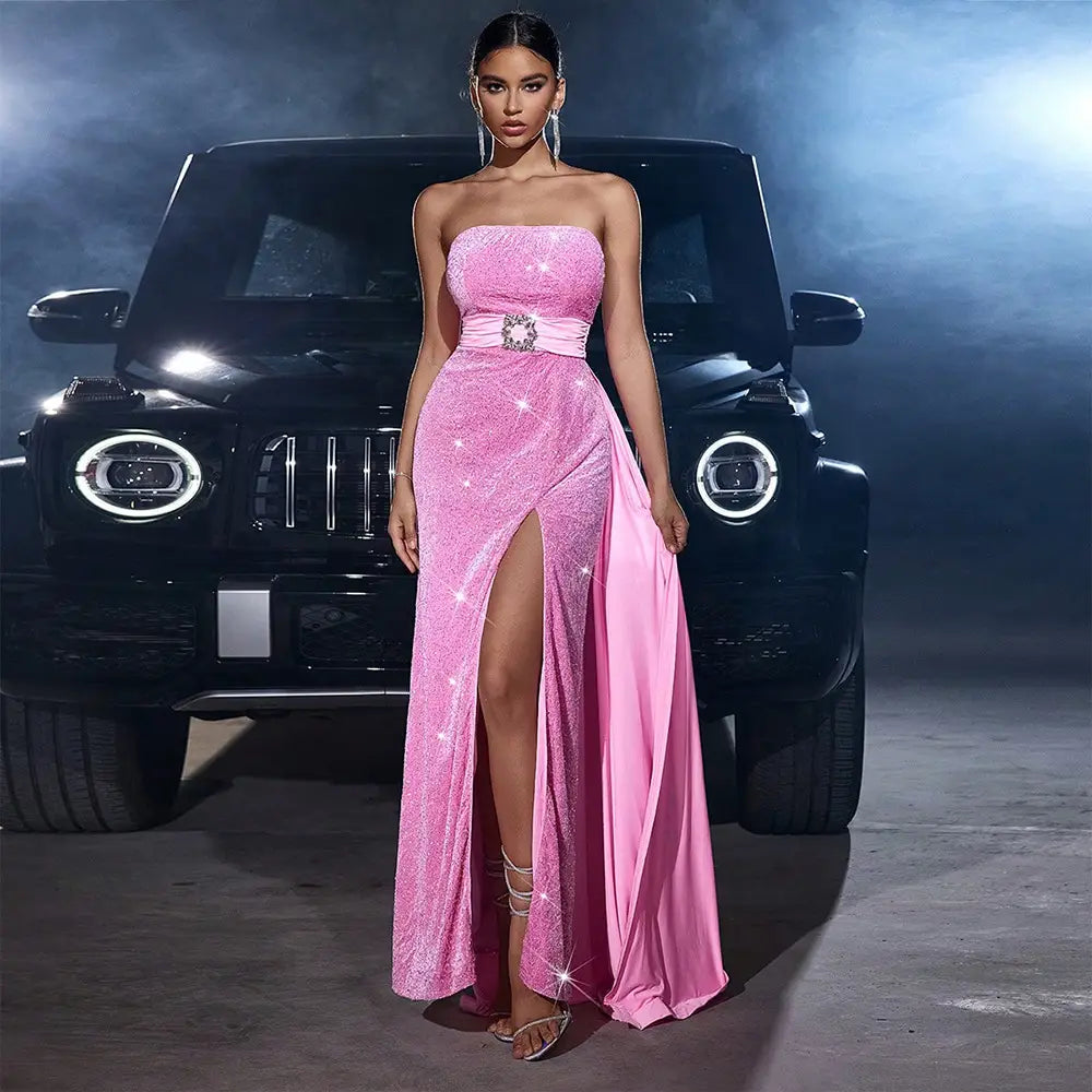 A shimmering pink velvet sequined cinched waist evening gown with a strapless design, high slit, sparkling embellishments, and a satin sash featuring a central crystal accent.