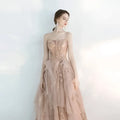 A female wedding gown in blush pink with intricate gold lace and layered champagne tulle toast skirts
