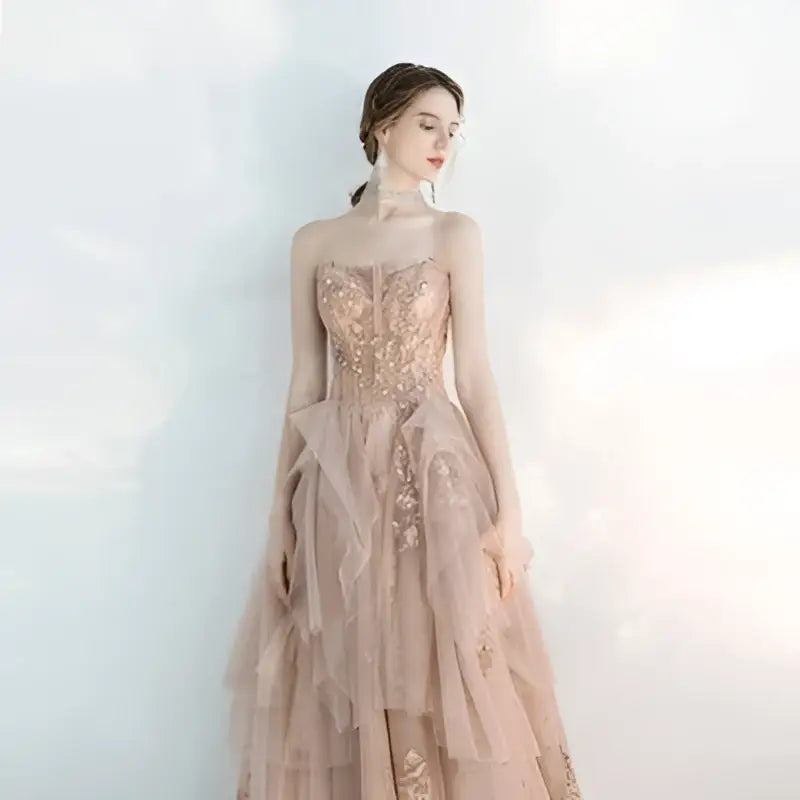 A female wedding gown in blush pink with intricate gold lace and layered champagne tulle toast skirts