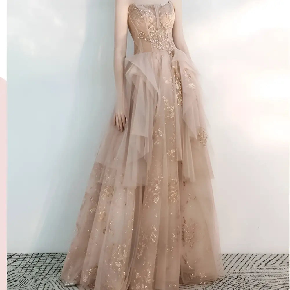 A strapless female wedding gown in champagne tulle toast with intricate gold embroidery and layered tulle fabric