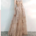 A female wedding gown in champagne tulle toast with intricate gold floral embroidery and a flowing layered skirt