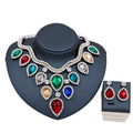 A colorful exaggerated bride necklace and earring set with multi-colored gemstones silver chain and rhinestone accents displayed on a black bust and sleek box