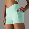 Cream high waisted athletic shorts in mint green with pocket design fitness feature holding a smartphone