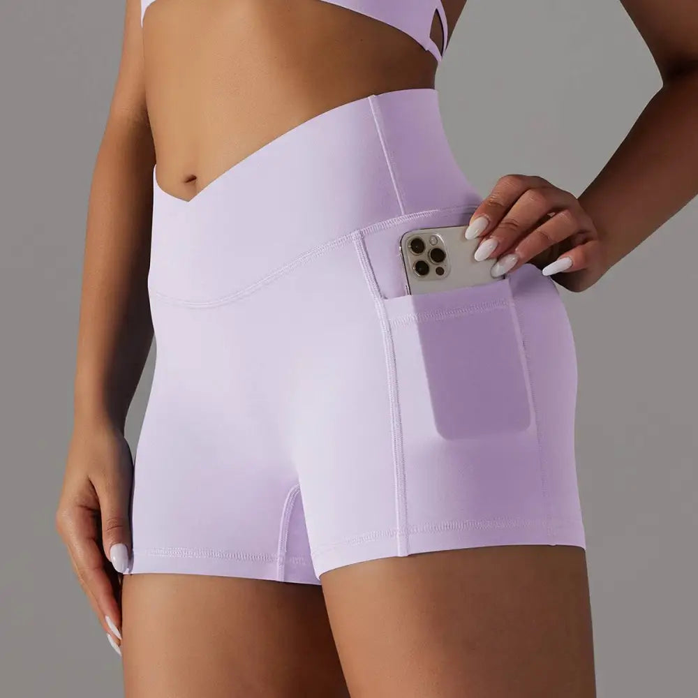 Lavender high-waisted athletic shorts with pocket design fitness features holding a smartphone for activewear use