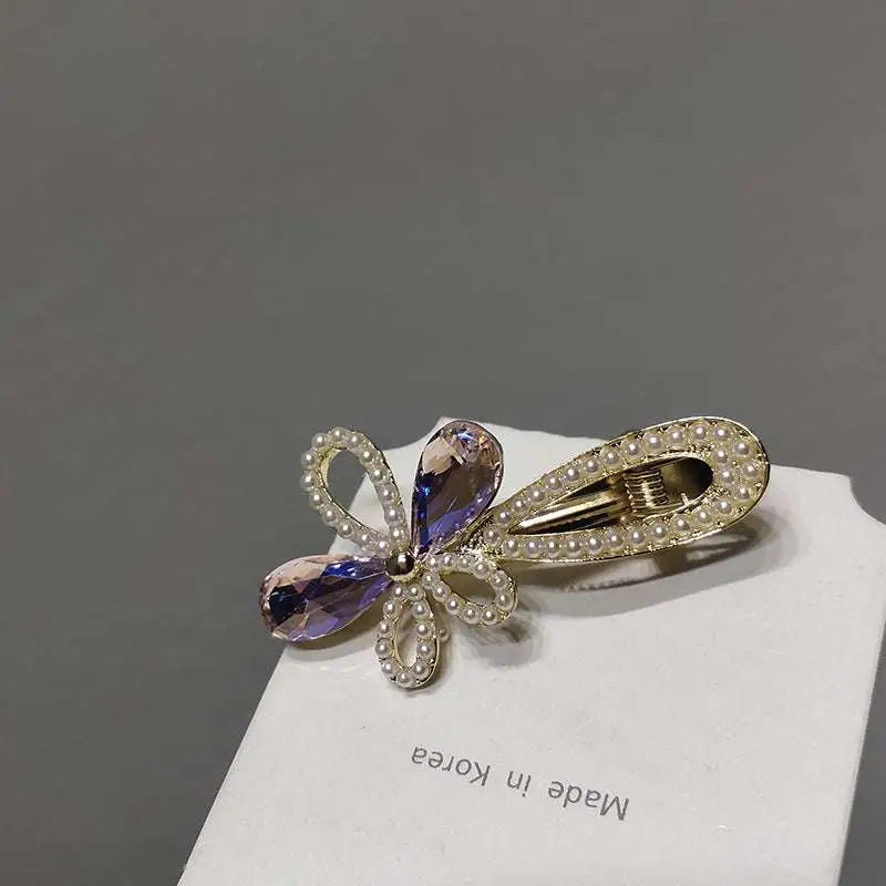 A gold-toned crystal daisy metal grab clip with purple teardrop crystals and white pearl bow design clip sweet accessory