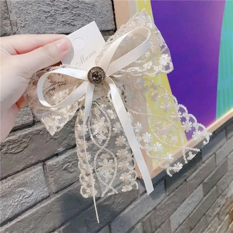 A delicate cream lace bow barrette with elegant crystal lace, a satin bow, and a central metallic button