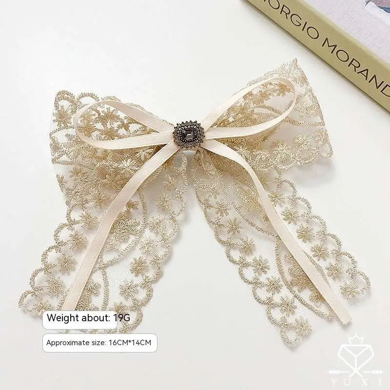 Elegant cream satin lace bow barrette adorned with intricate gold lace and a sparkling black central metallic button