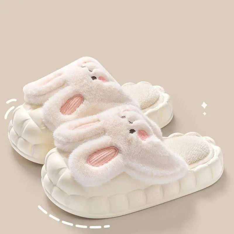 Soft white plush bunny slippers with pink inner ears and embroidered black eyes, featuring a cushioned sole.