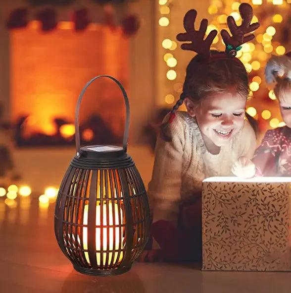 Black woven rattan lantern with a solar panel on top and a warm glowing light inside designed for solar retro patio use.