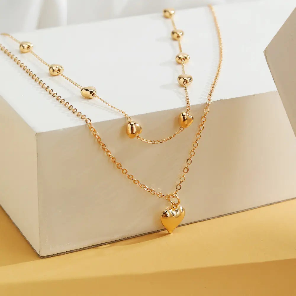 Gold-toned double layer heart pendant fine chain necklace featuring delicate chain links with spherical heart-shaped beads and a larger dangling heart pendant.