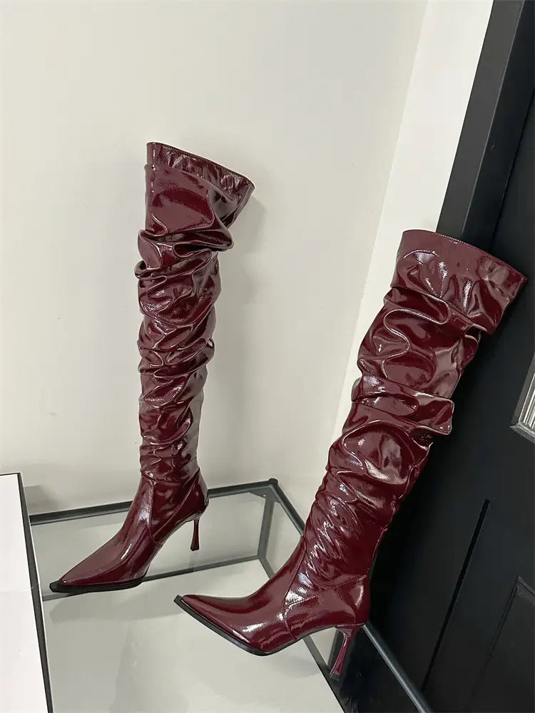burgundy patent leather over-the-knee boots with a ruched glossy texture and pointed toe, featuring an autumn stiletto heel in a heel pile style design.
