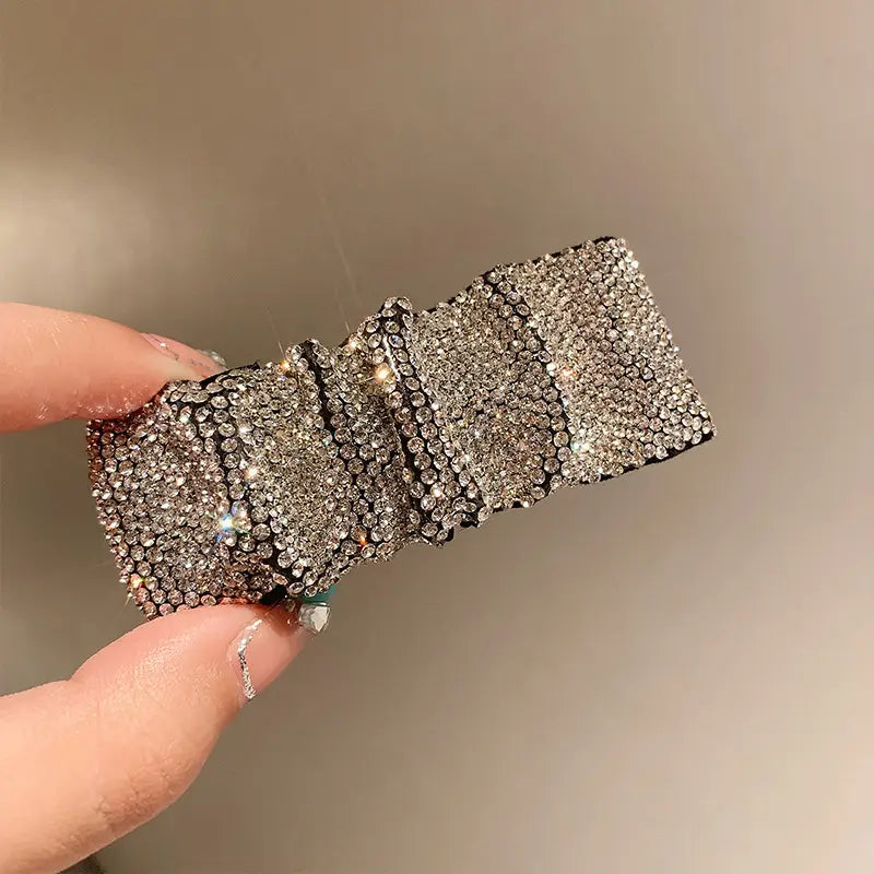 A silver pleated bb clip features a sparkling rhinestone bow with a sleek, structured design and hot rhinestone details.