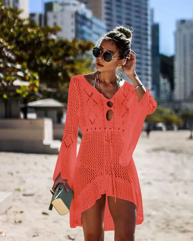 A vibrant coral-colored long-sleeved crochet bikini women swimsuit cover-up dress with v-neck and asymmetrical hemline.