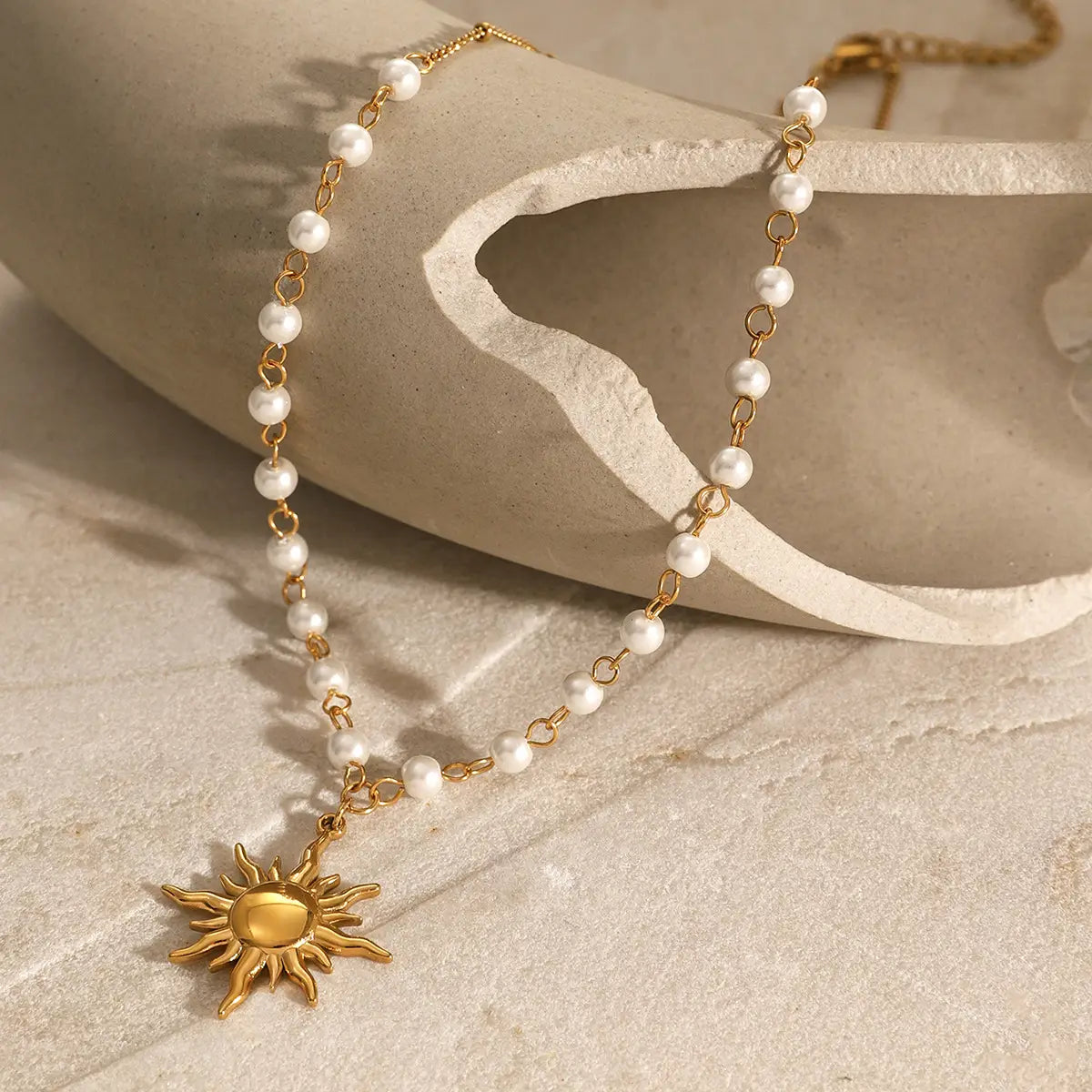 A delicate stainless steel pearl necklace featuring small white pearls and a gold-toned sun pendant with radiating rays.