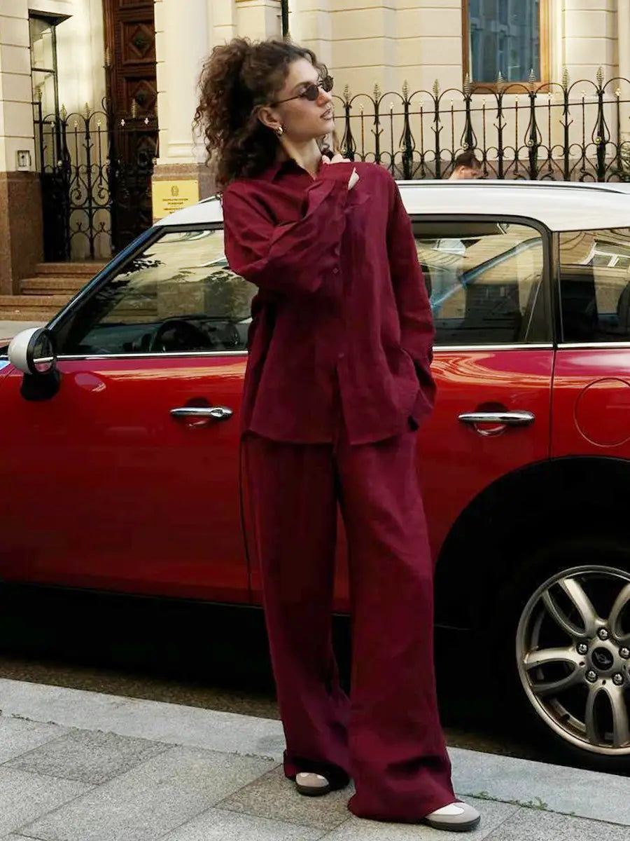 a woman wearing a maroon long sleeve cotton shirt trousers suit with oversized button-up shirt and wide-leg trousers paired with white slip-on shoes