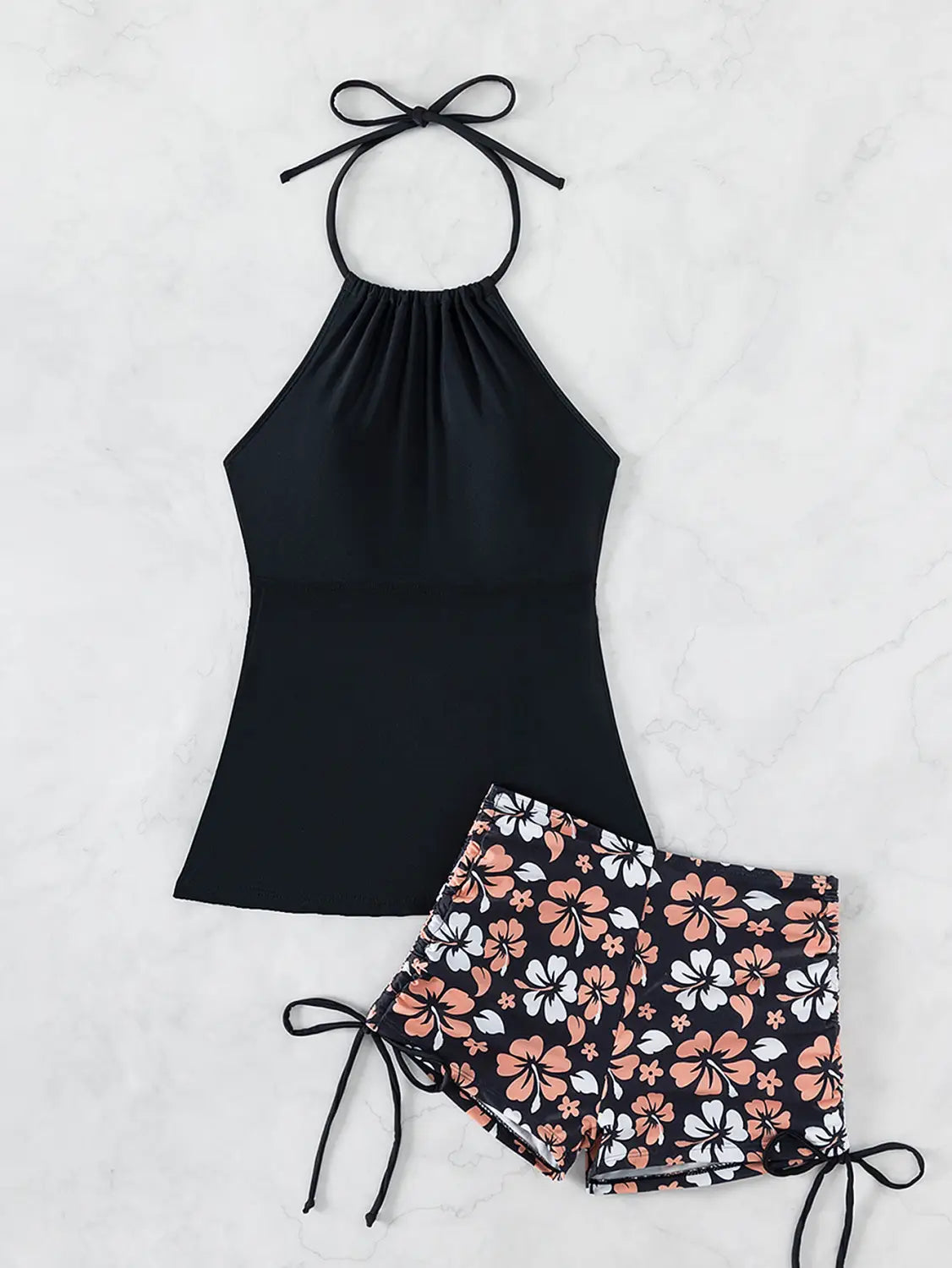 black halterneck printed halter split swimsuit featuring a halter top with gathered neckline and tie-back paired with floral-patterned shorts with peach and white hibiscus flowers on a dark background
