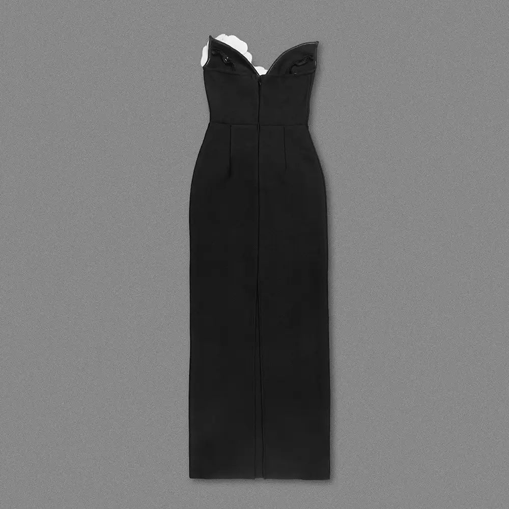 black backless bandage gown with a fitted silhouette featuring white floral embellishments at the backless bandage chest and subtle vertical pleats along the front.
