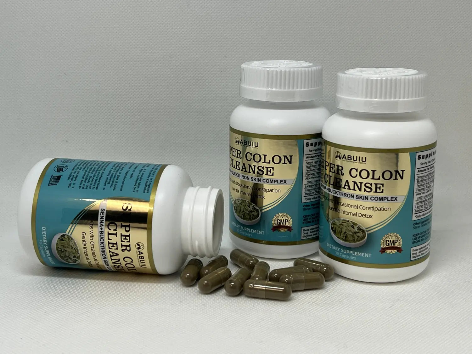 three white plastic bottles of abuiu super colon cleanse dietary supplement with gold and teal labels and brown capsules displayed for cleanse capsule use.