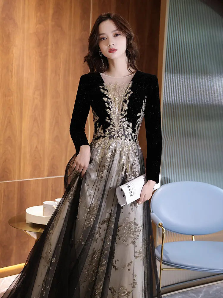 Black moderator long sleeve evening gown in black and gold featuring intricate beaded embroidery on the bodice and a sheer layered skirt for annual party wear.