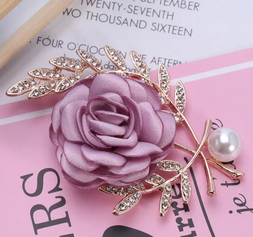 A delicate lavender satin rose fabric flower lady brooch adorned with gold-toned leaves crystals and a pearl from the flower lady temperamental pin floral brooch set.