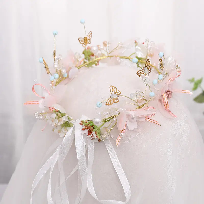 A delicate pink floral bridal wreath adorned with gold butterfly charms, pearl beads, and sheer ribbon ties for luxury women’s fashion.