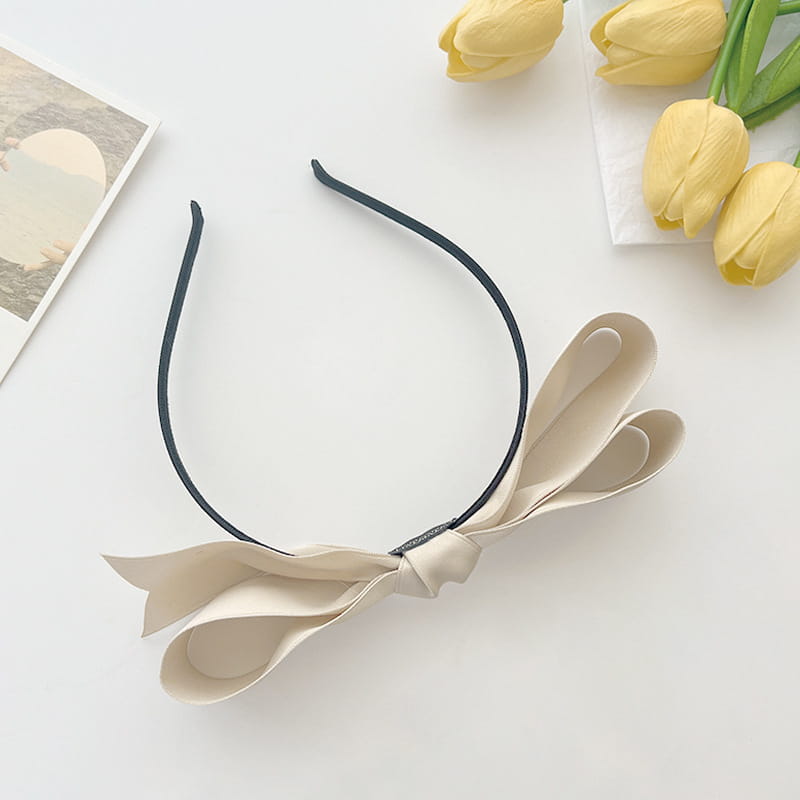 A delicate beige french satin bow headband for women with a sleek black elastic band.