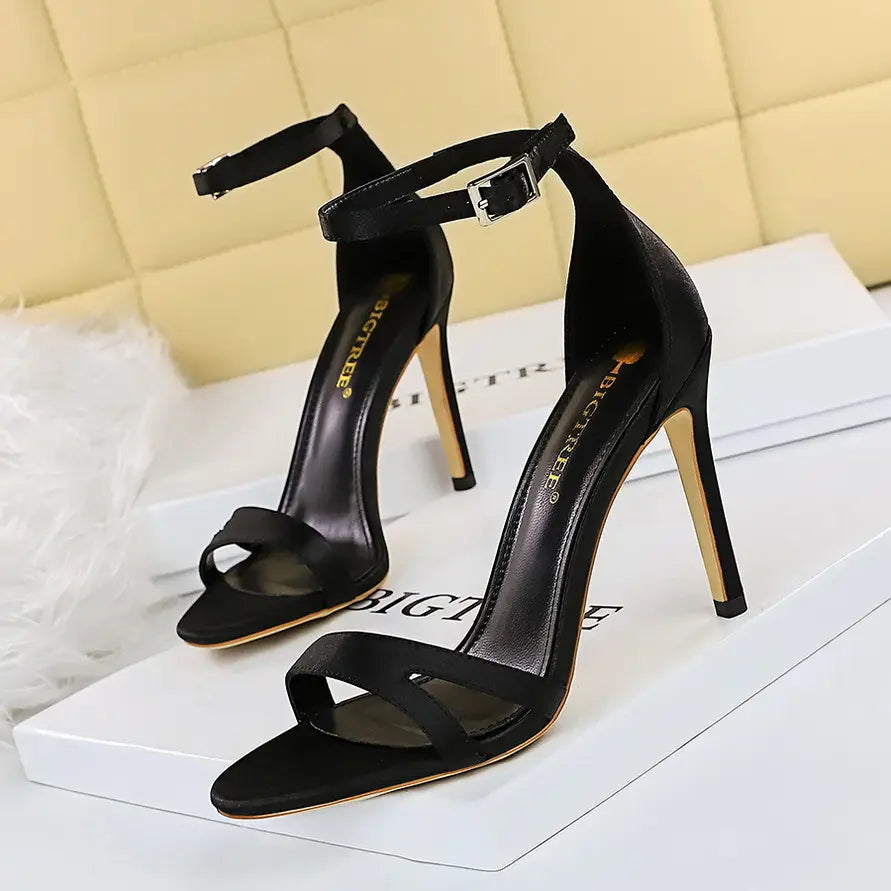 Black satin high heel toe cutout sandals featuring a sleek minimalist design and gold-toned heel toe satin accents.