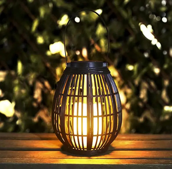Black woven rattan lantern with a handle glowing warmly from within designed as an explosive solar retro patio lighting solution.