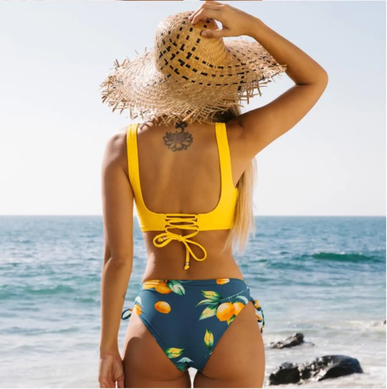 Yellow bikini swimsuit featuring a two-piece design with a citrus fruit print in yellow and navy blue and side ties.