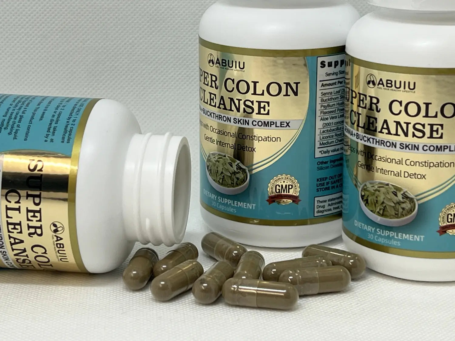 White plastic bottle with gold and teal label reading super colon cleanse by abuiu lying on its side next to two upright bottles in a 30 count cleanse capsule product for digestive health.
