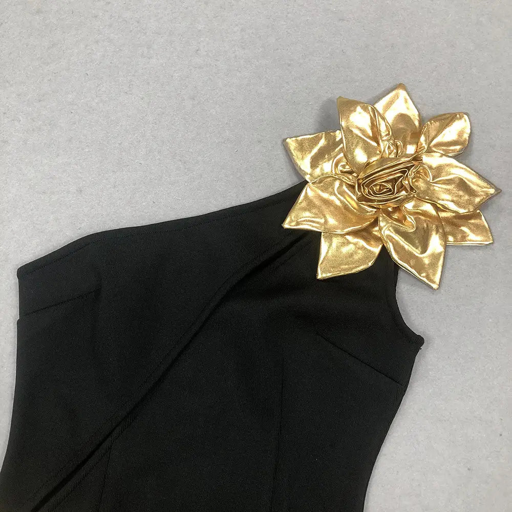 Black satin bandage golden flower maxi dress featuring a one-shoulder design and a shiny gold fabric flower embellishment.