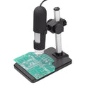 Black handheld digital usb microscope camera with silver accents on adjustable arm capturing green circuit board details