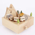A light-colored wooden diy dancing music box featuring a christmas train with engraved track and carved trees and mountains