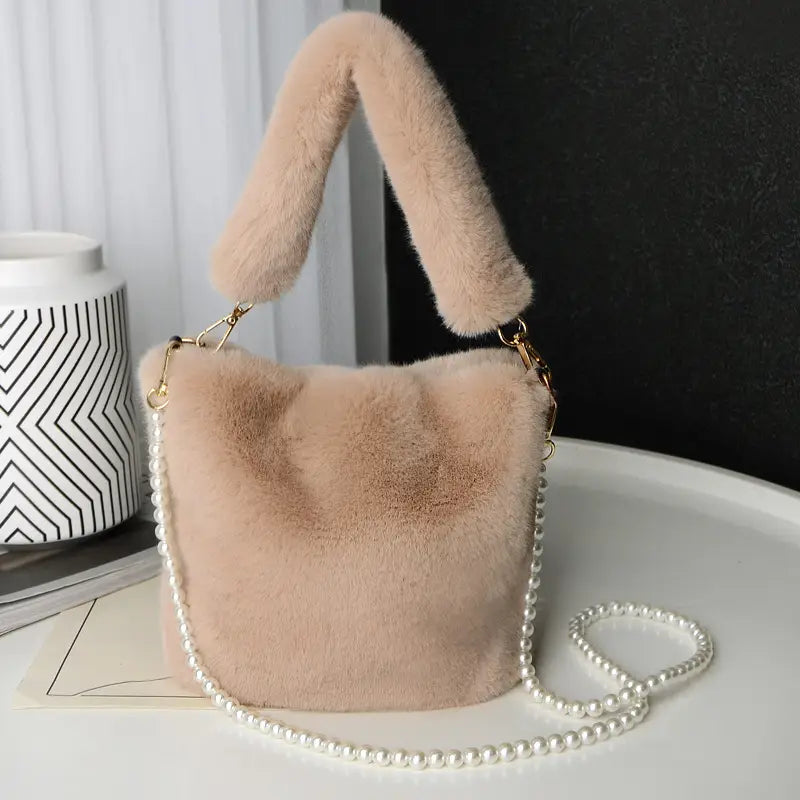 A soft blush-colored checkerboard plush bucket bag made of faux fur featuring a matching fluffy handle and a delicate pearl chain design strap.