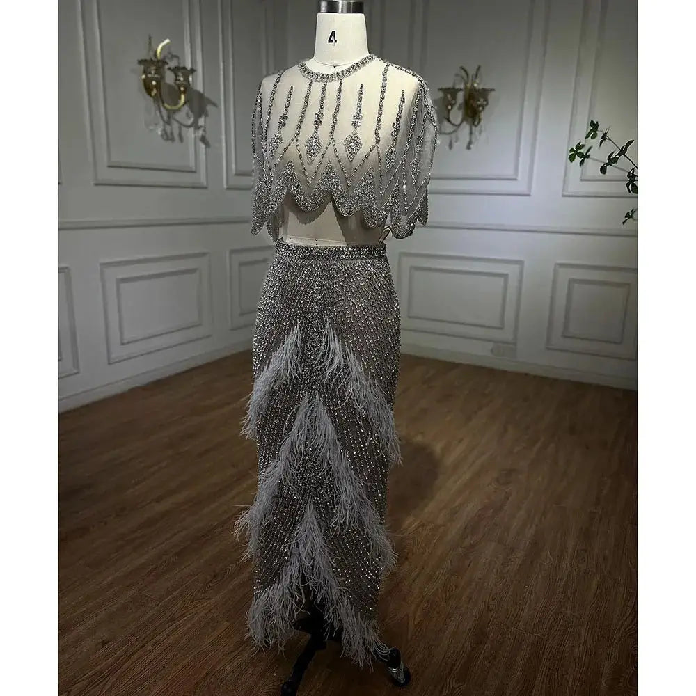 A shimmering silver nude two-piece evening dress with silver beaded detailing and feather accents on the skirt displayed on a mannequin.