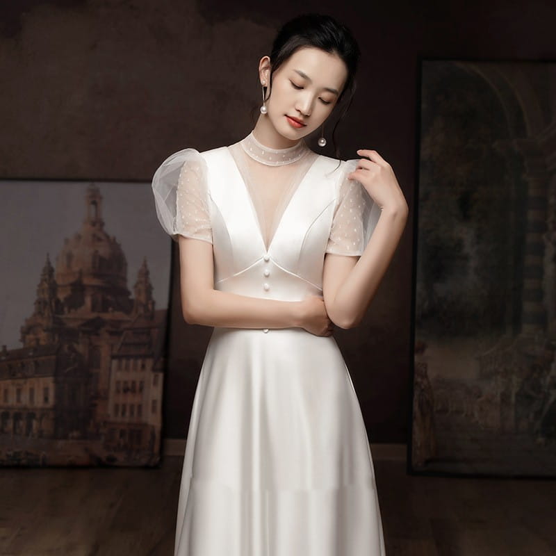 A woman wears a white satin wedding dress with sheer puff sleeves and delicate pearl detailing ideal for a white engagement wedding dress.