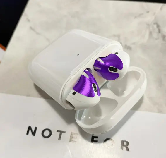 white apple airpods 2 with purple metallic ear tips in a charging case featuring a gold glossy custom sticker skin.
