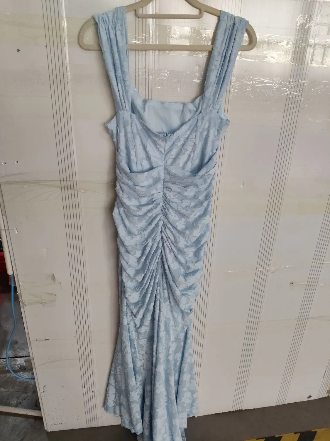 A light blue sleeveless mermaid-style dress with a ruched bodice and subtle floral pattern displayed on a wooden hanger is a stylish alternative to a pink sexy evening dress with ruched bodycon fit suitable for women purple sleeveless collections.
