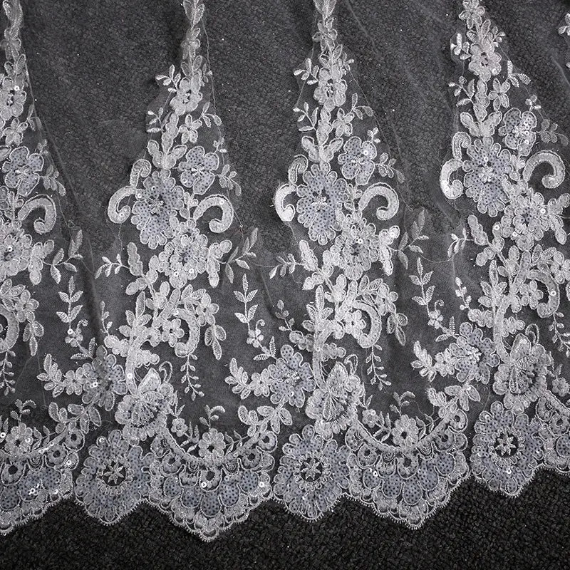 Delicate white lace wedding dress trailing floral bridal veil featuring intricate floral and scrollwork patterns accented by subtle silver sequins.