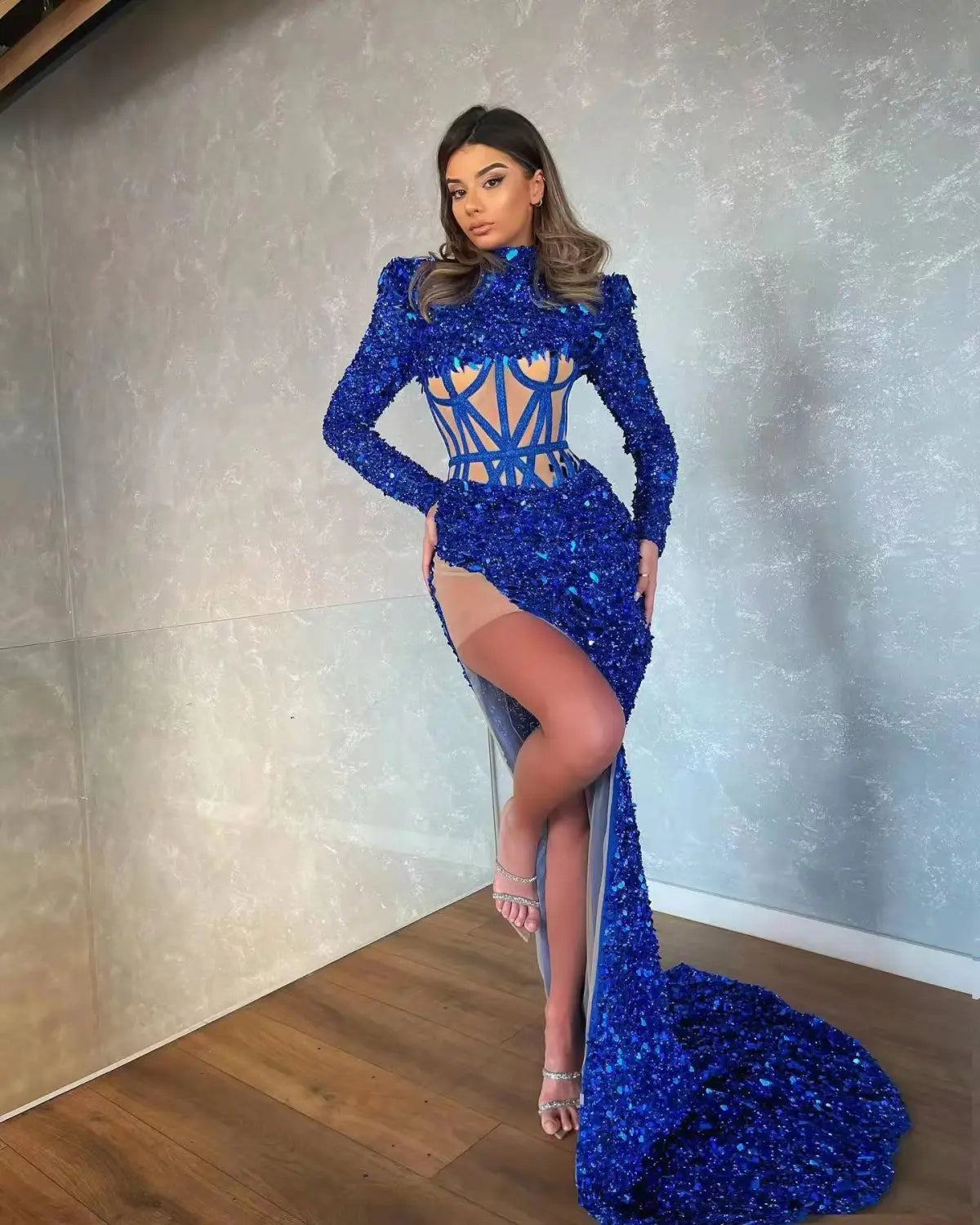 A dazzling royal blue siren ji sequin gown featuring a high neckline long sleeves geometric cutout bodice and a high slit.