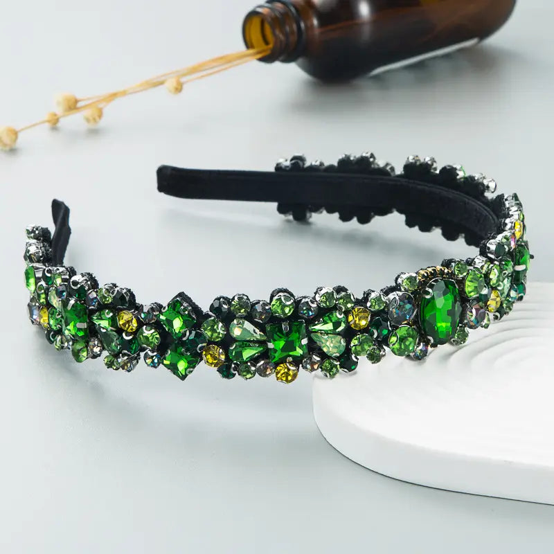 A black baroque vintage court style headband decorated with an intricate array of green and yellow crystals in oval teardrop and round cuts.