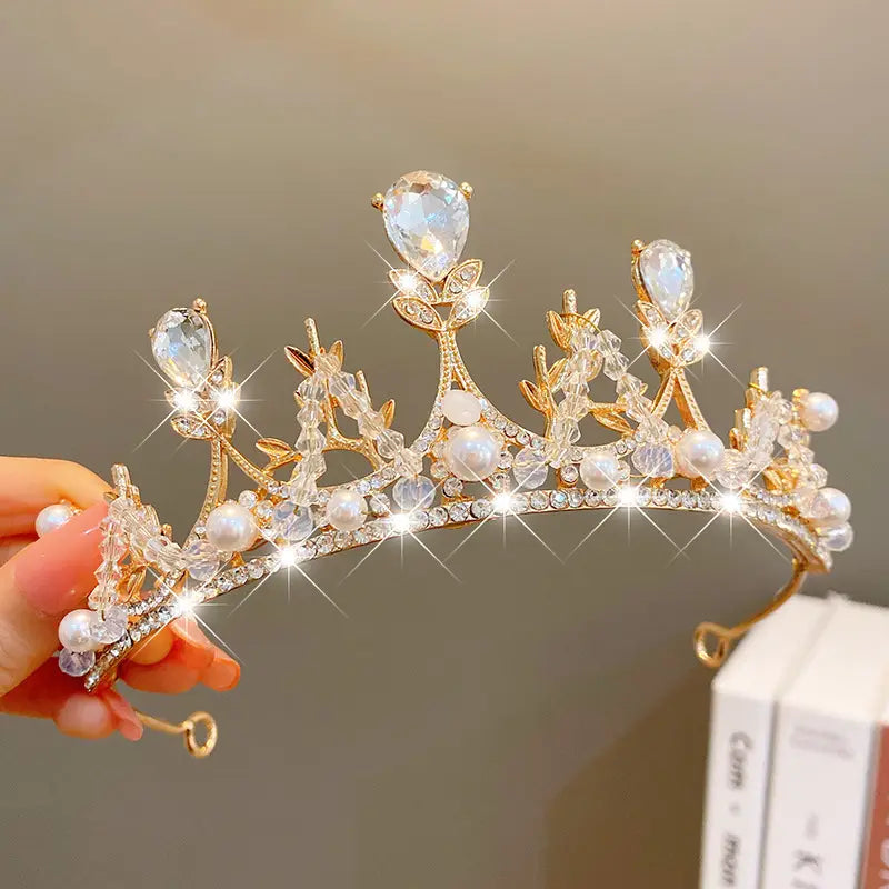 A delicate gold crown headband from sweet fashion jewelry featuring sparkling clear crystals, pearlescent white pearls, and intricate leaf-like metalwork as elegant hair accessories.