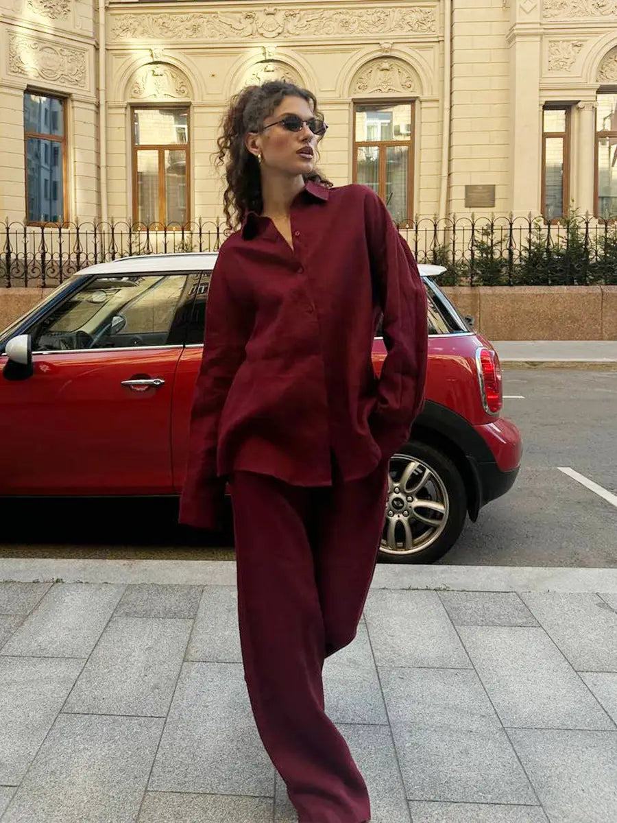 A woman wearing a matching maroon cotton long sleeve shirt trousers suit styled in an oversized relaxed fit.