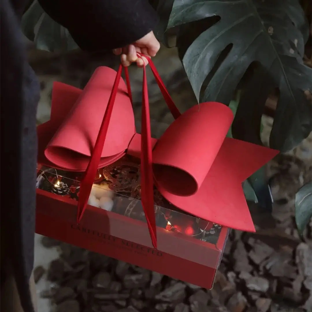 A vibrant red bow knot handheld flower box with glossy layered paper bow attached to a matching gift box with clear window.